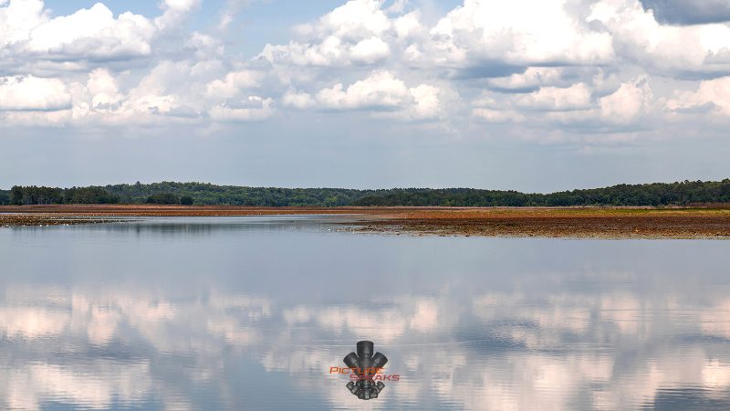 Clouds reflect atop a lake as a thin strip of land sits in the backdrop.